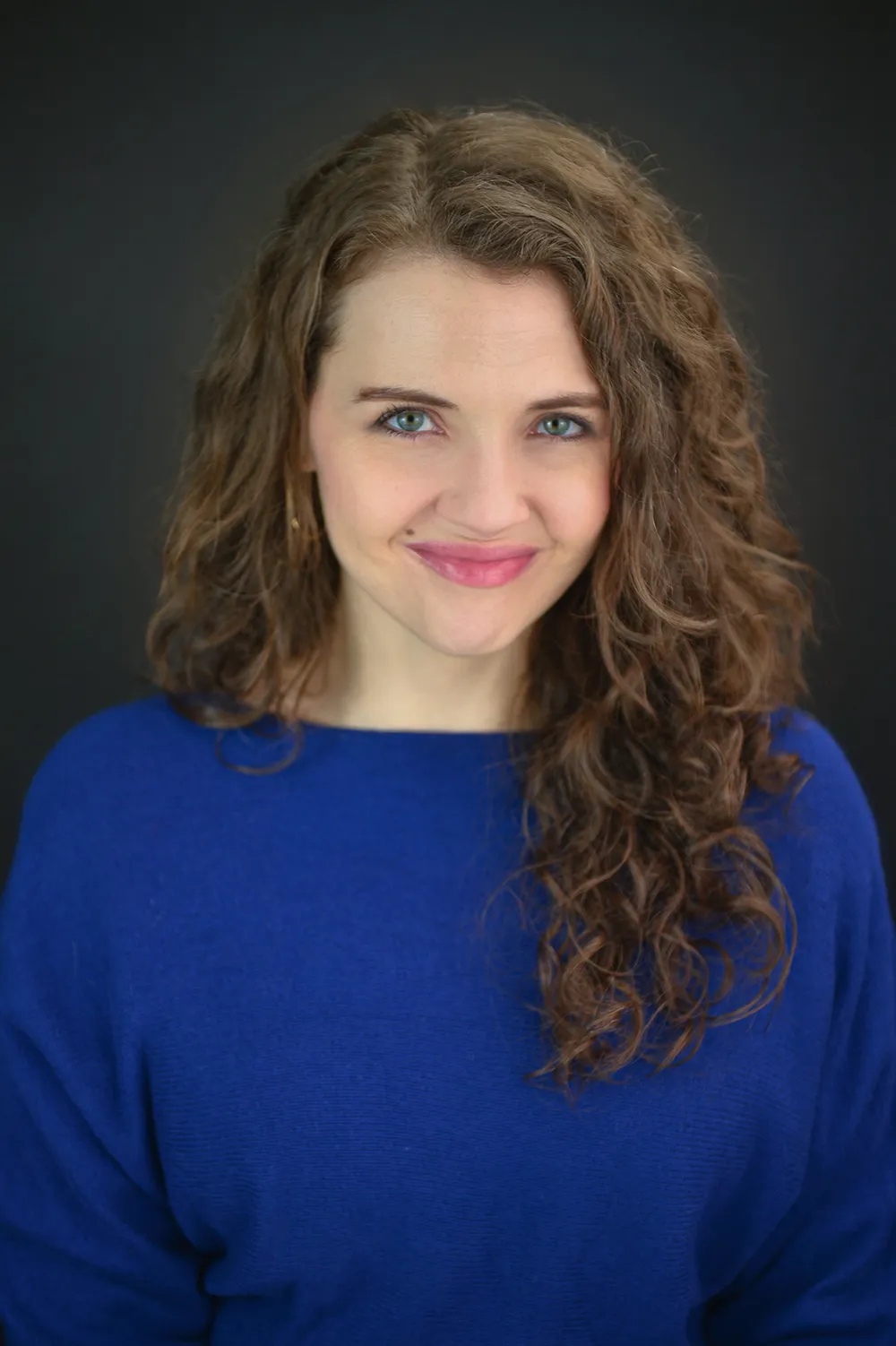 Author Kayla Rae Whitaker, she has curly long brown hair and she is wearing a blue top.